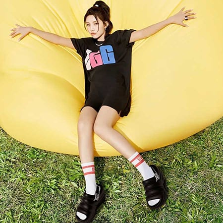 girl wearing black UGG tshirt and Black UGG slides, lying on yellow inflatable