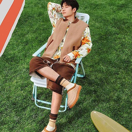man in brown loungewear and floralshirt sitting on deckchair wearing ugg slippers